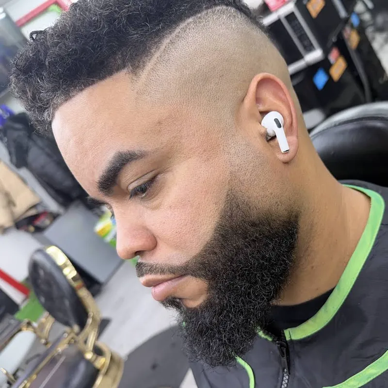High skin fade with a curly top, sharp line-up and full beard